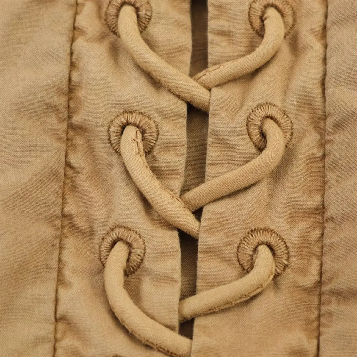 Close-up of the side lace-up grommet detail on the camel-colored ruffled top