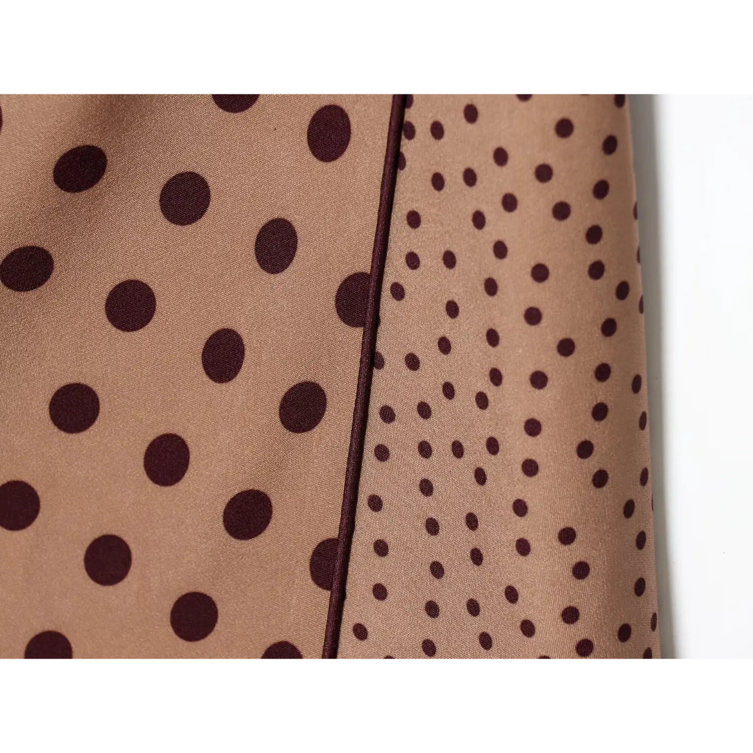 Close-up stitching seam between large and tiny dark polka dot fabric panels on camel midi dress
