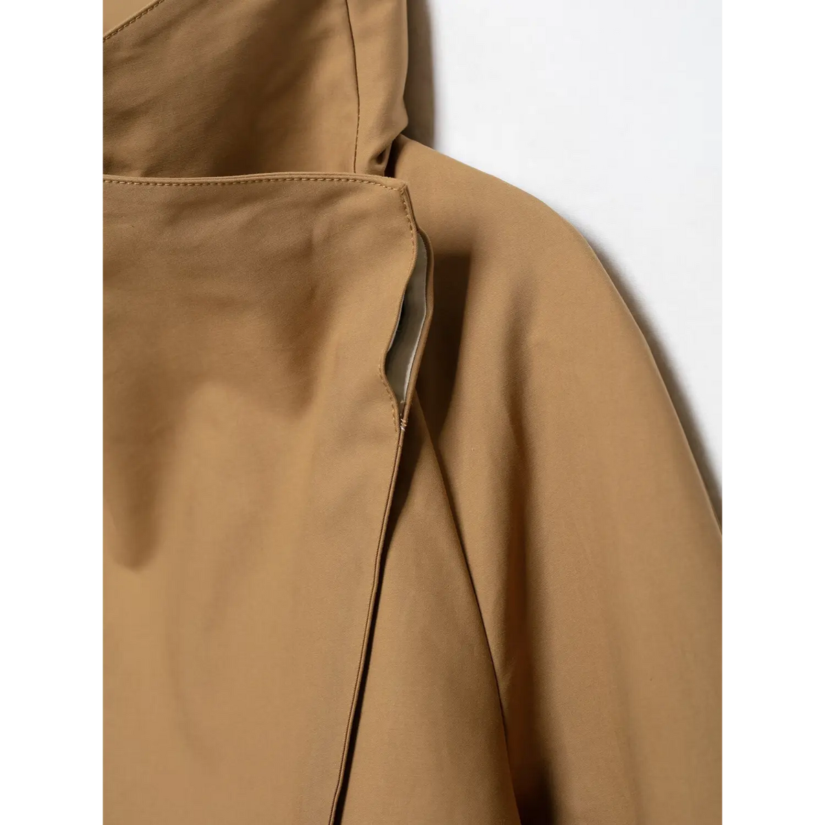Macro detail of camel jacket side slit pocket, showing fabric seam and pocket lining edge
