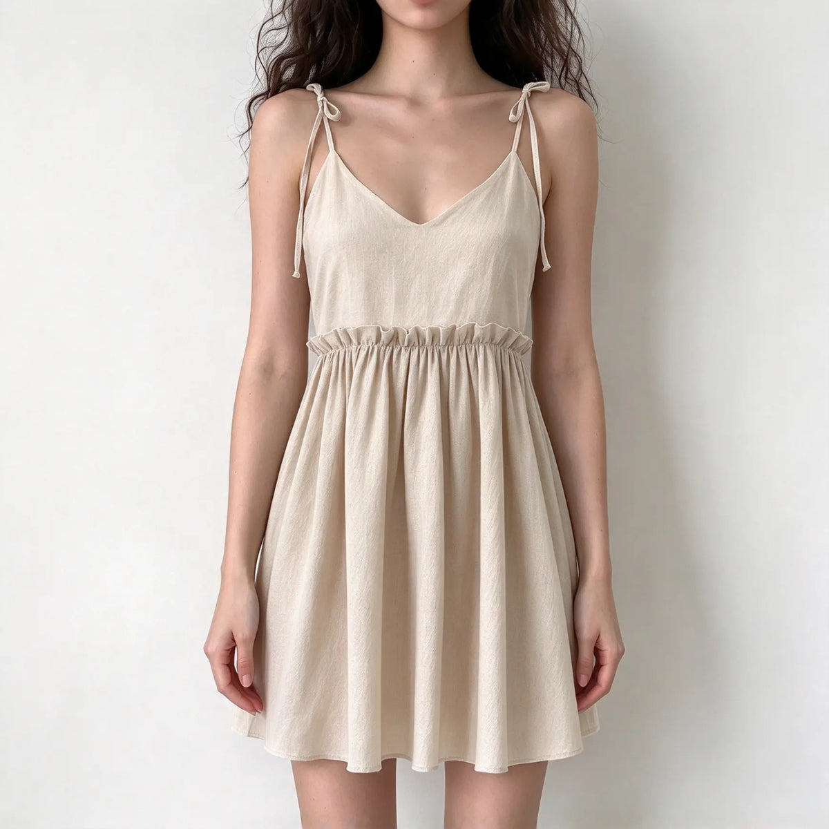 Model wearing camel tie strap babydoll ruffle waist mini dress, front view