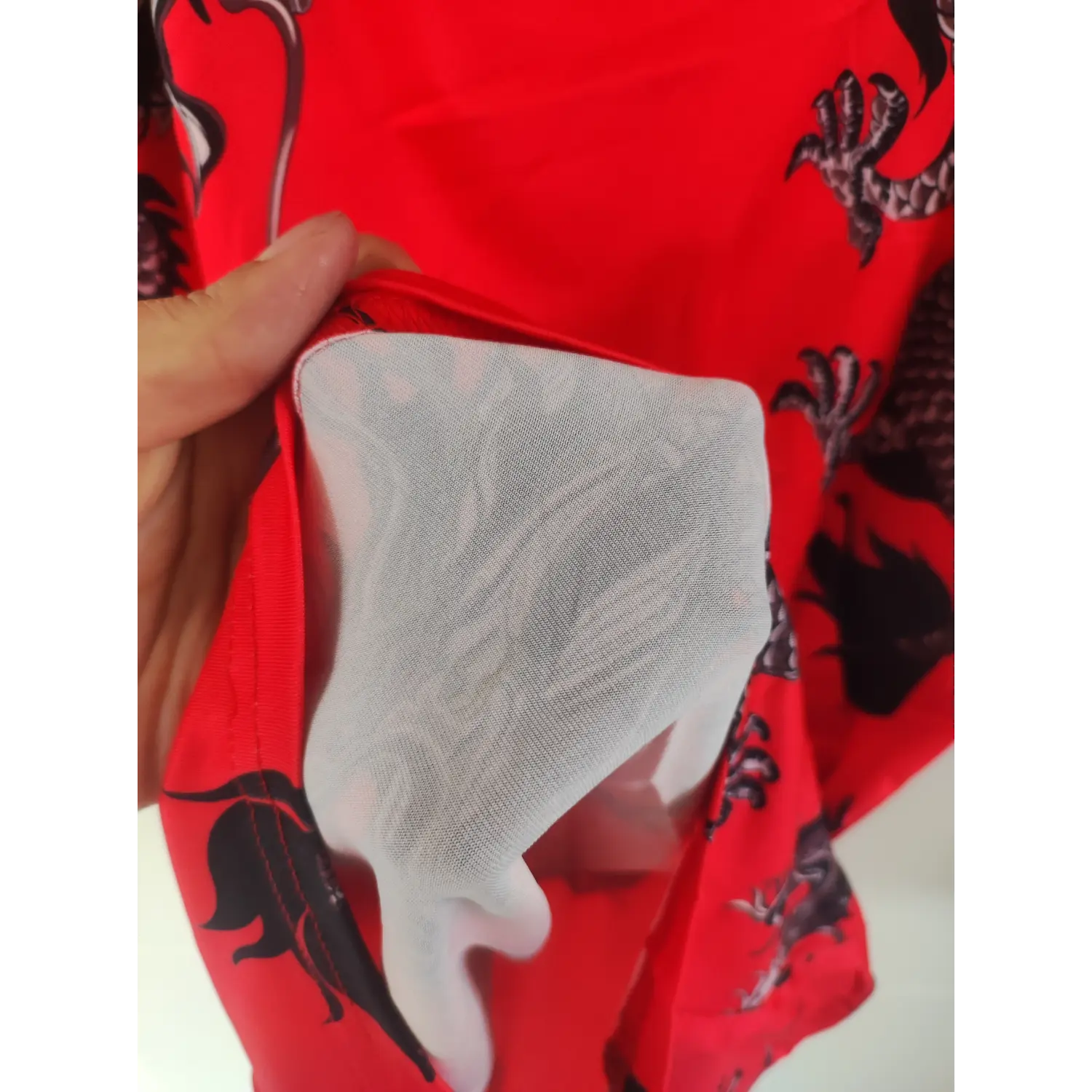 Close-up hem detail, white inner lining of red dragon print spaghetti strap dress