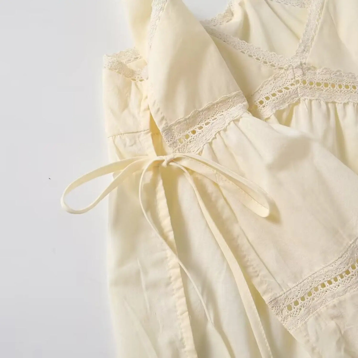 Close up shot of cream babydoll cami top, showing side drawstring tie and eyelet lace trim