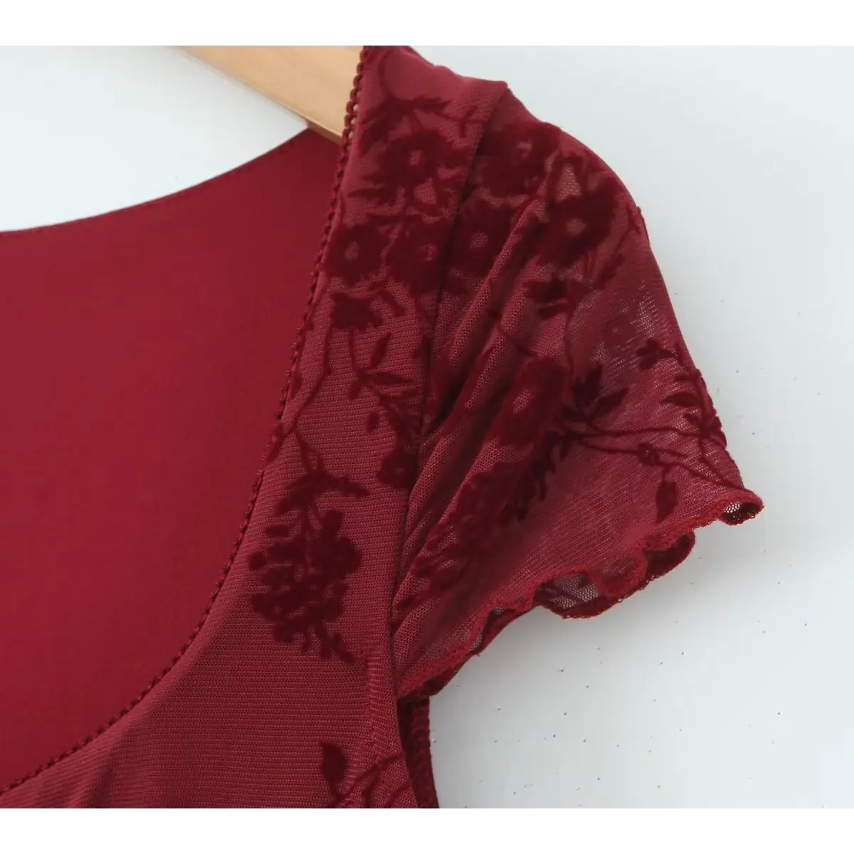 Close-up of the cap sleeve and neckline on a burgundy flocked floral mesh dress, highlighting the scalloped edge and flocked floral pattern.
