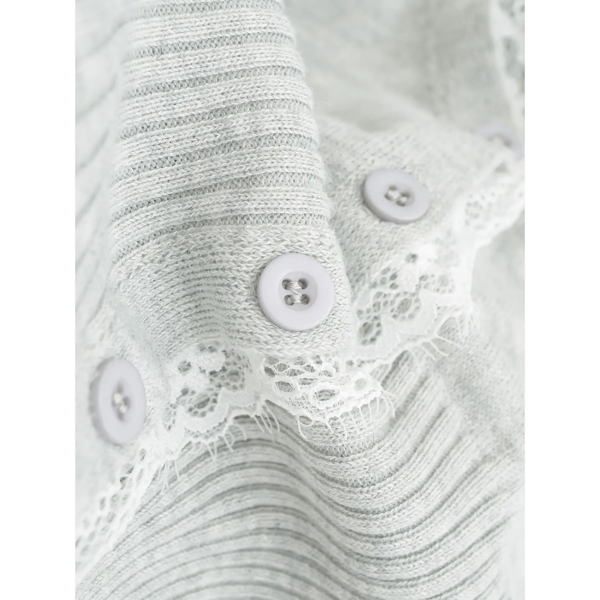 Macro shot of round buttons and frayed white eyelash lace along cardigan front placket, soft heather knit
