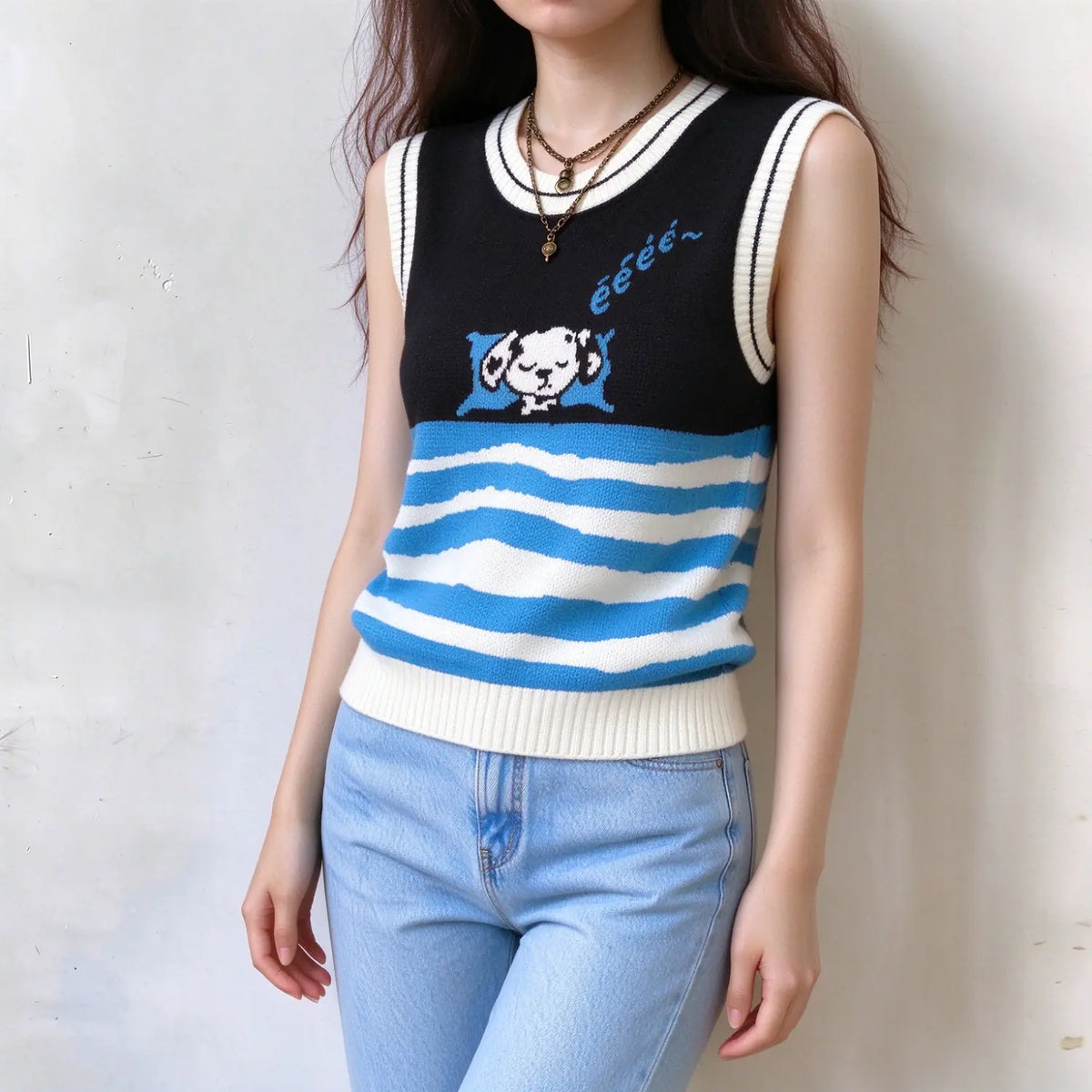 Back view of female model wearing sleeveless knit vest, solid black upper back, blue and white wavy striped lower back, white ribbed neck and arm trim