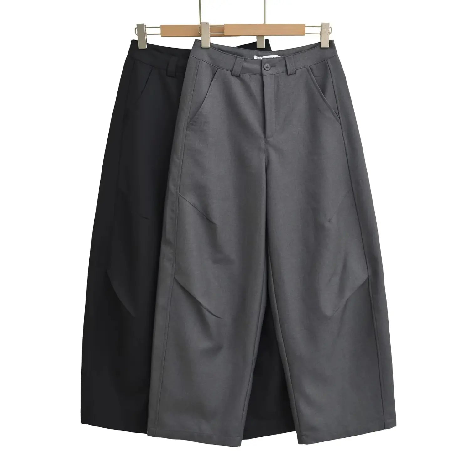 Charcoal gray and black draped wide leg dress pants hung on wooden hanger, retail display photo