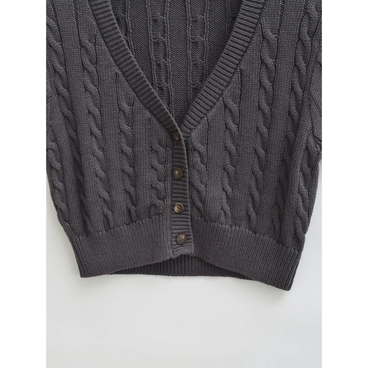 Close-up of the ribbed hem and cable knit pattern on the charcoal gray cardigan.
