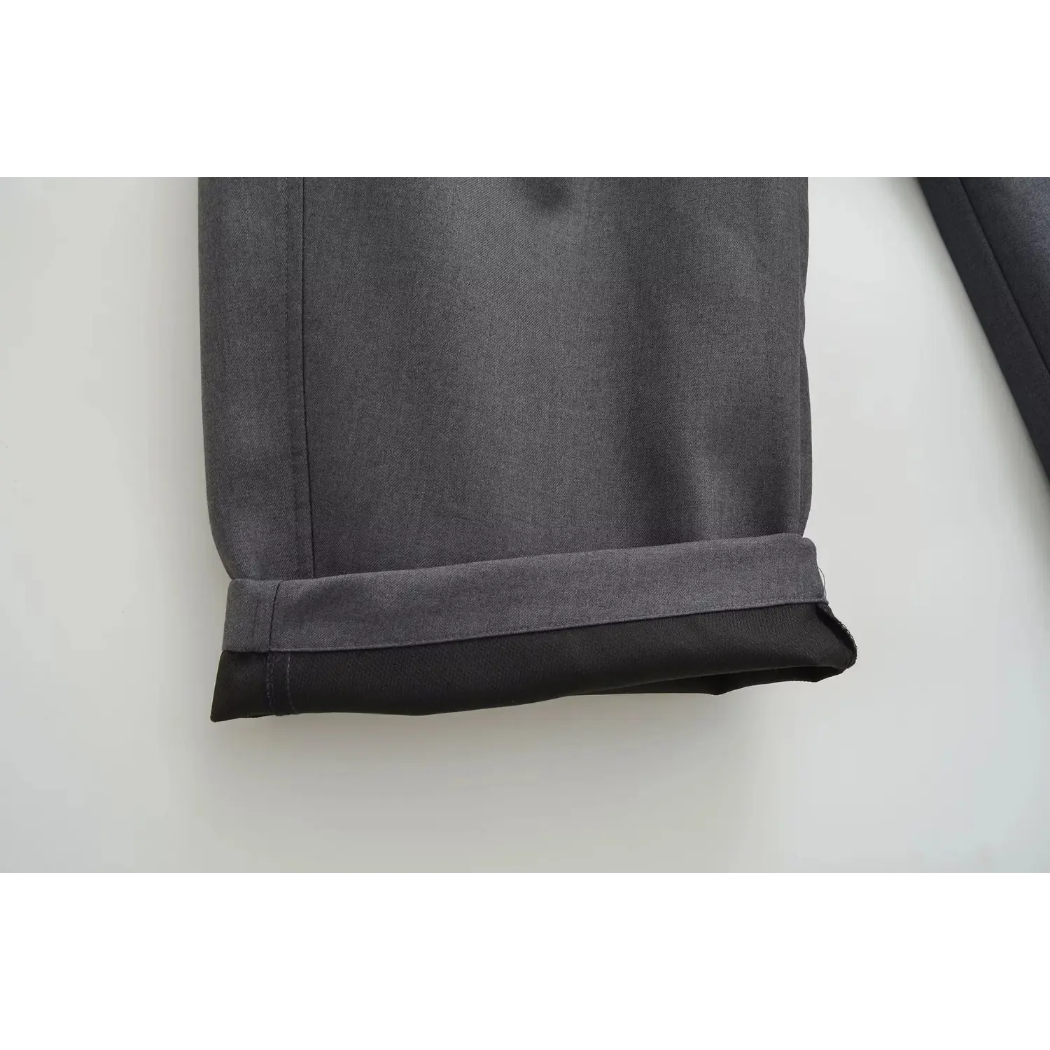 Close-up shot of charcoal gray wide leg trousers folded hem, show inner lining and neat stitching detail