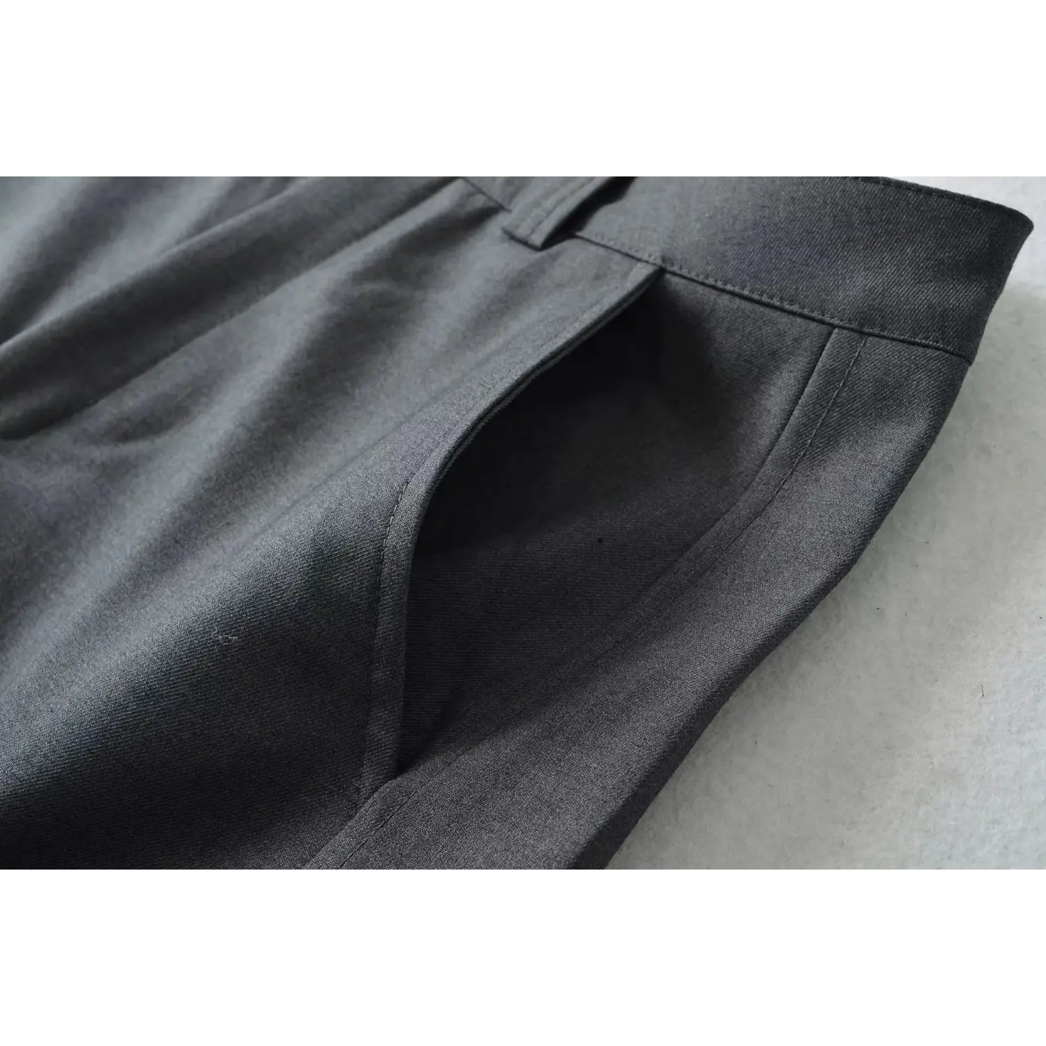 Macro close-up of charcoal gray wide leg suit trousers front slant pocket, show neat stitching and woven twill fabric detail
