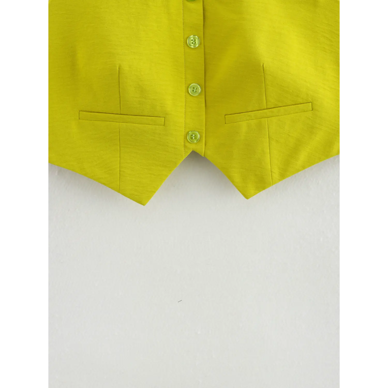 Close-up of pointed V hem and pocket stitching on chartreuse cropped one-shoulder vest