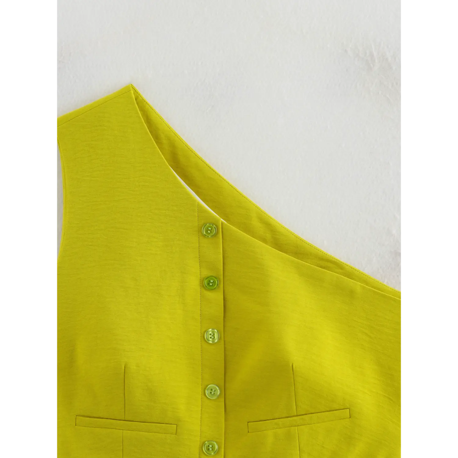 Close-up of front button placket and faux pocket detail on chartreuse asymmetric single shoulder waistcoat