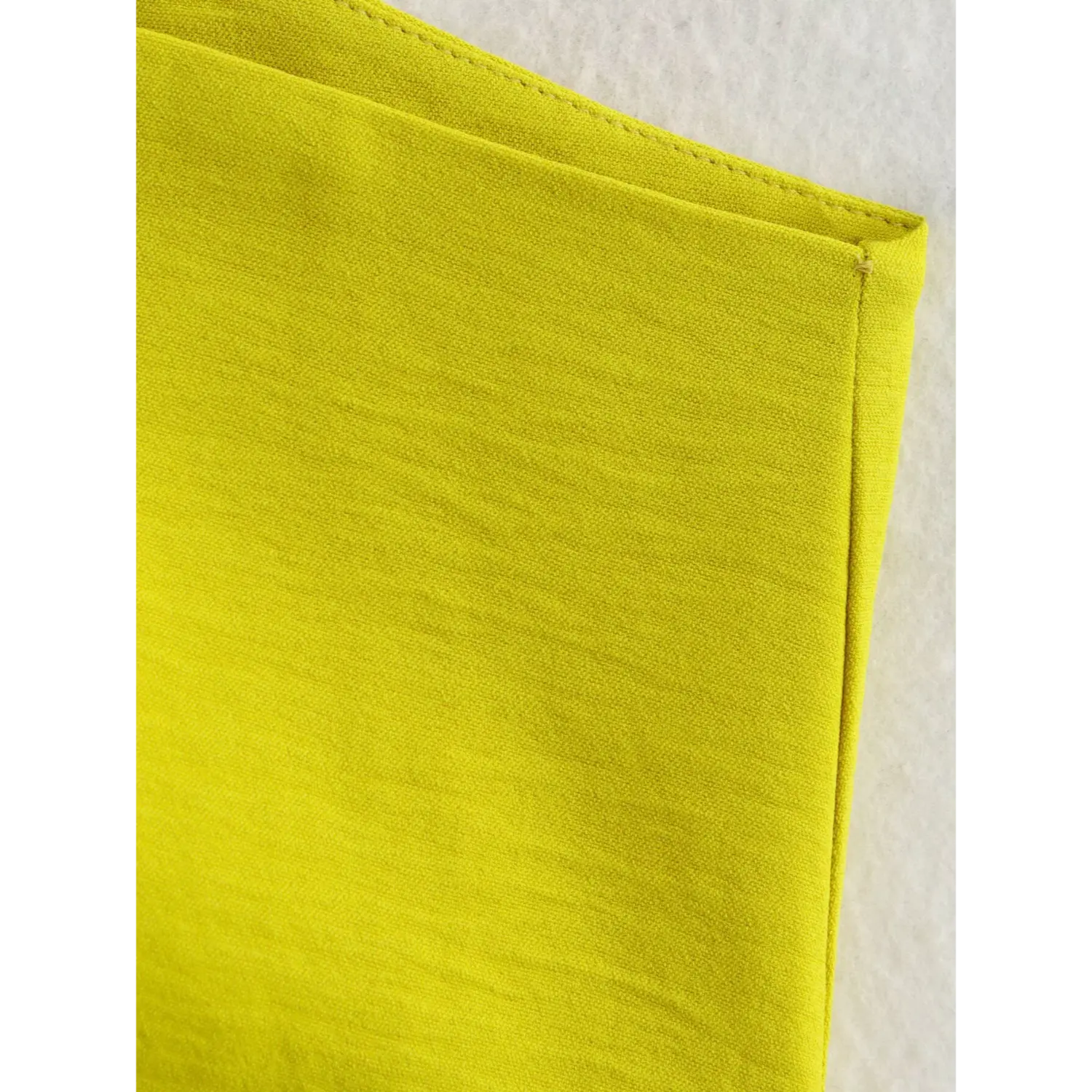 Extreme close-up of textured woven fabric on chartreuse asymmetric waistcoat