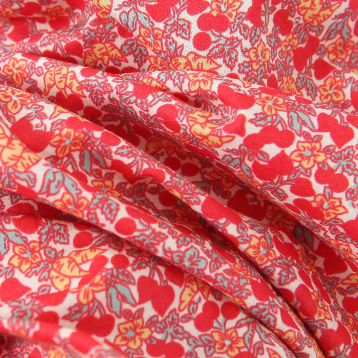 Macro close-up of lightweight woven fabric with vintage red cherry, small flower and green leaf allover print on off-white base.
