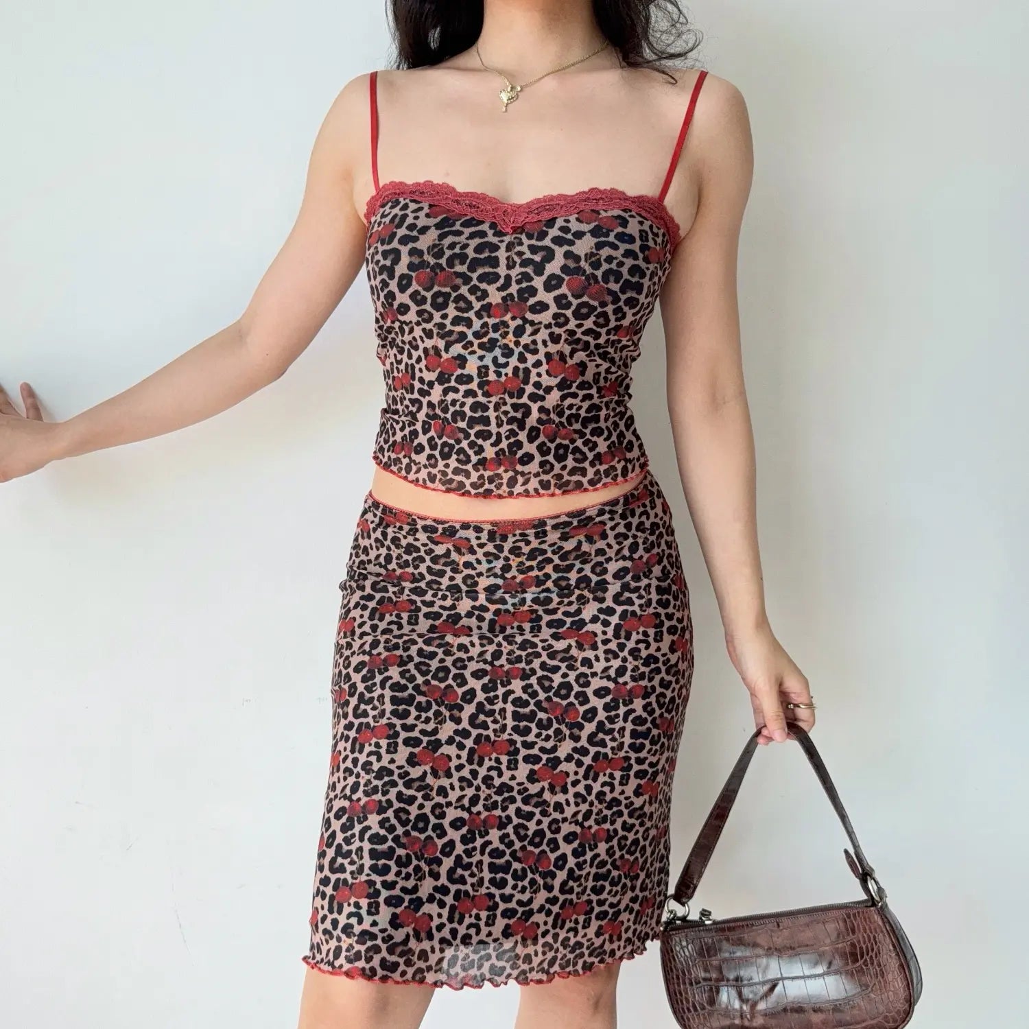 Front lifestyle shot on model of mesh two piece set with leopard & cherry print, lace trim camisole, fitted midi skirt with wavy hem edge