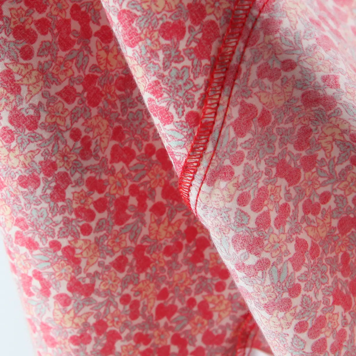  Close-up of red elastic overlock stitching on cherry floral woven fabric, neat inner garment seam workmanship.