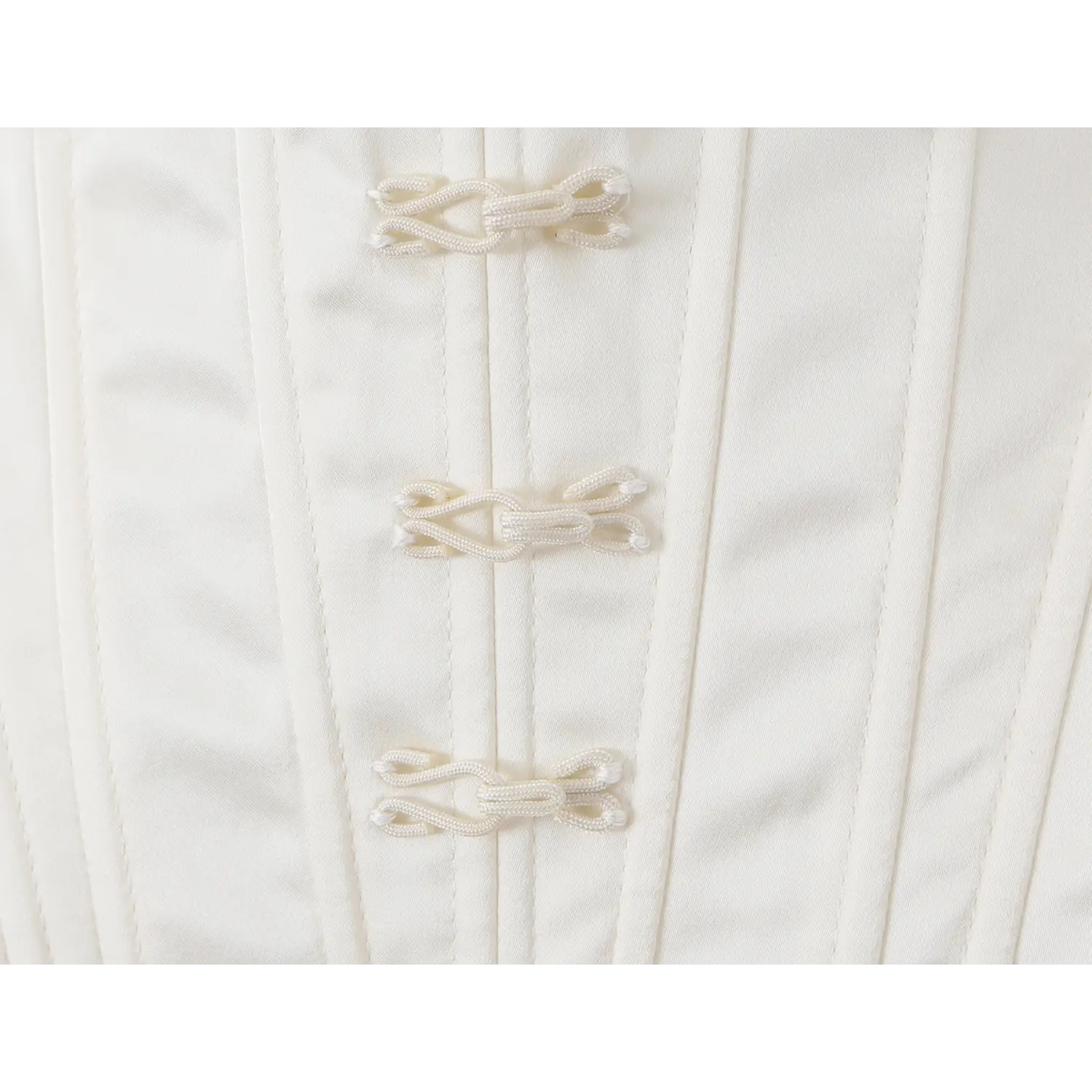 Close-up view of woven Chinese frog knot buttons on front of white structured corset camisole