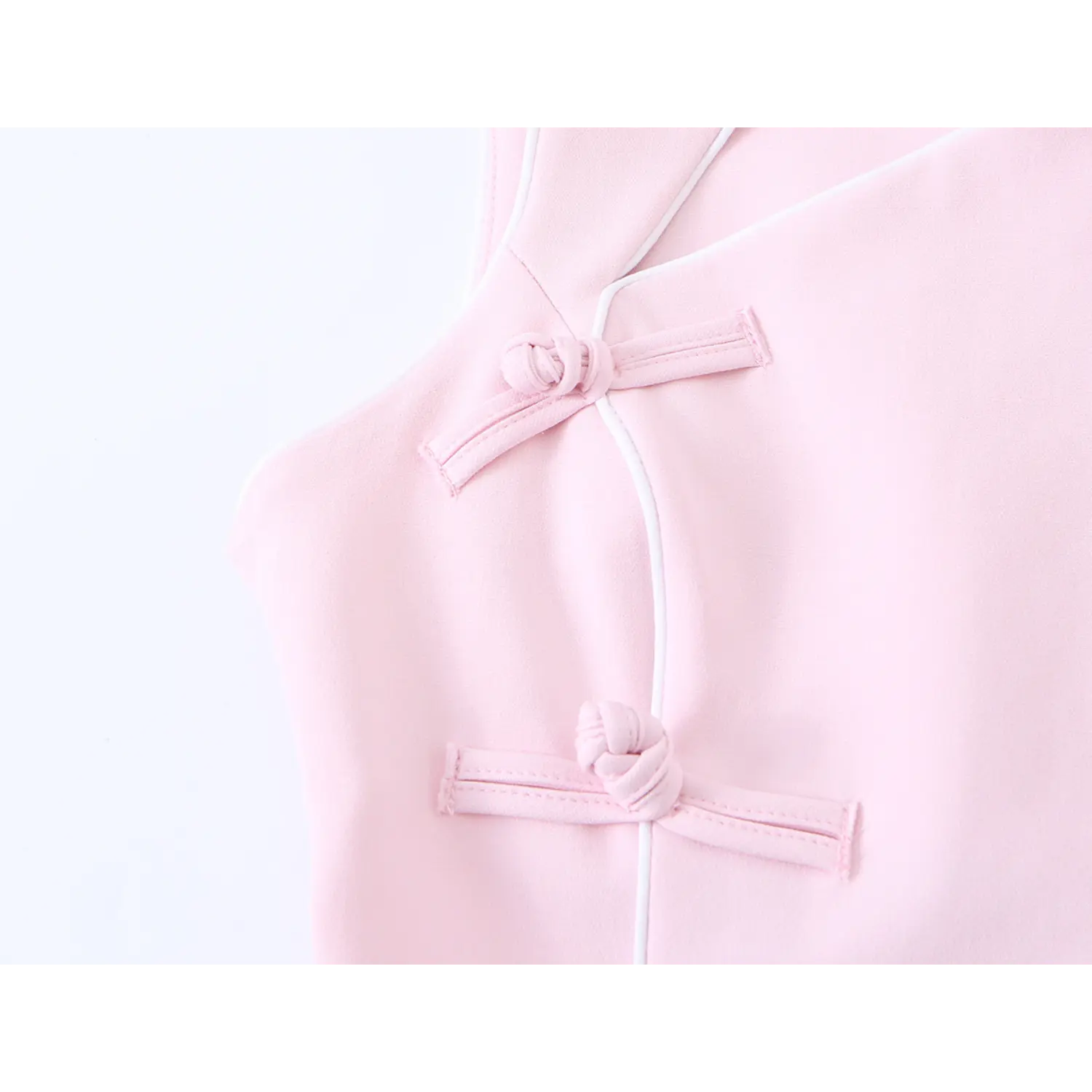 Macro detail of matching pink fabric frog buttons and thin white piping edge on modern sleeveless qipao