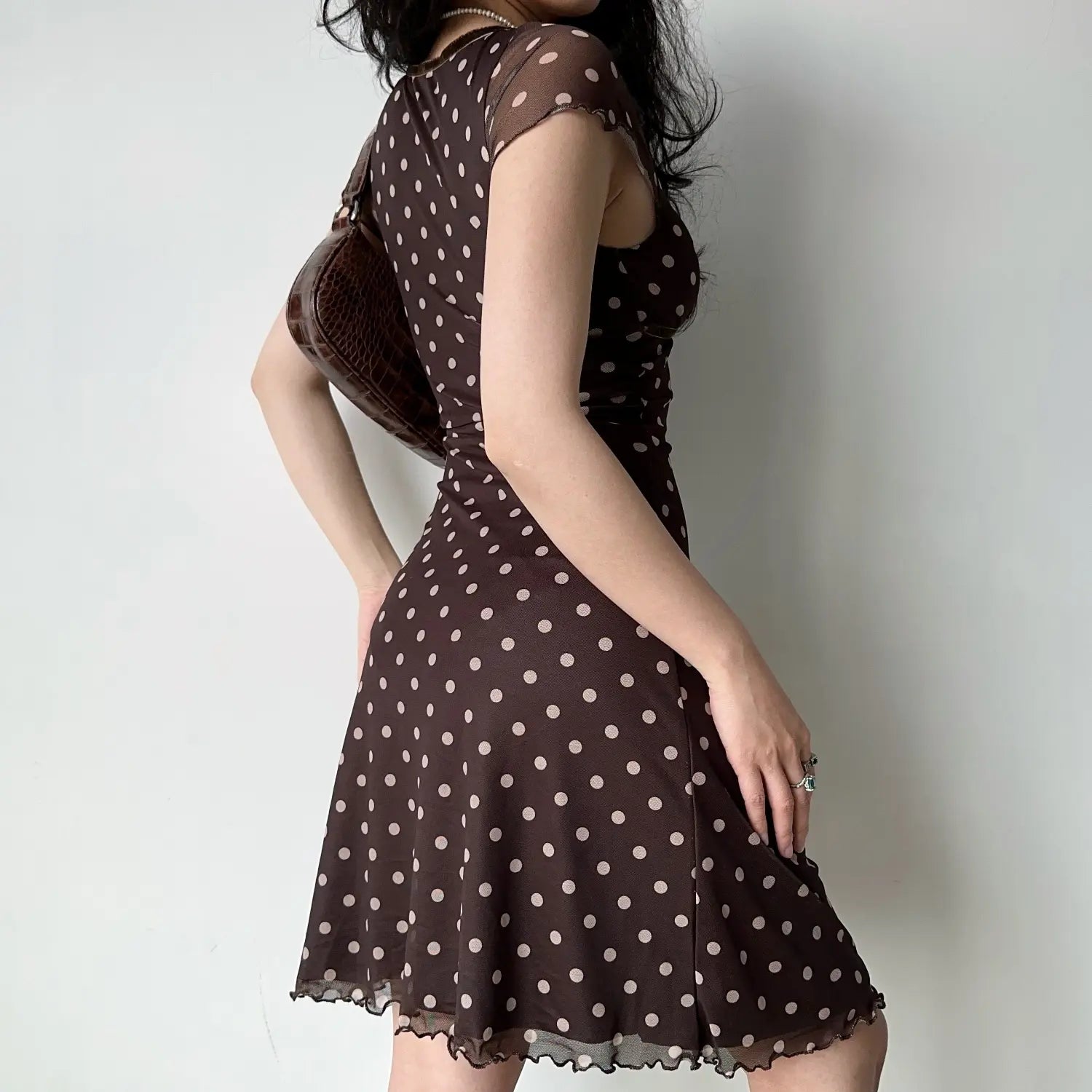 Model back three‑quarter view chocolate brown polka dot mesh midi dress short cap sleeve fitted waist ruffle lettuce hem