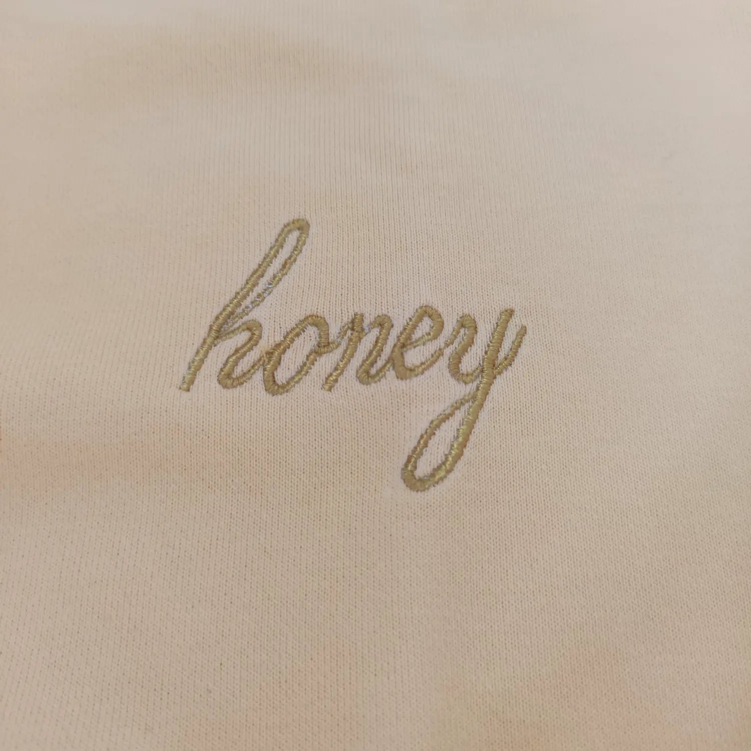 Close-up detail golden honey cursive embroidery on yellow sweatshirt chest