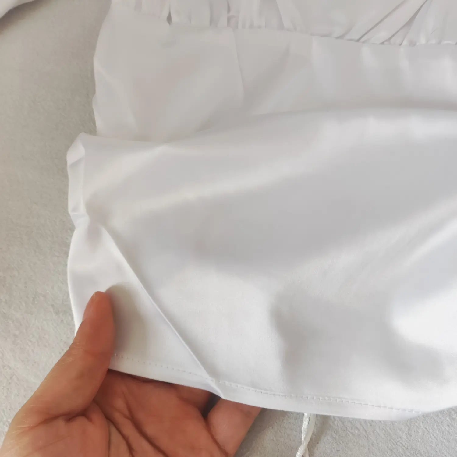 Close up texture of smooth white satin fabric and neat bottom hem stitching