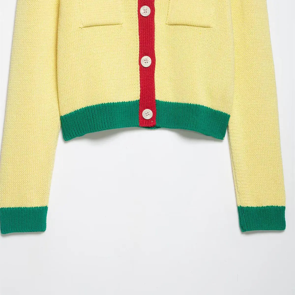 Close-up of the hem and button placket on the color-block cropped knit cardigan, featuring yellow body, red trim, green hem, and white shell buttons