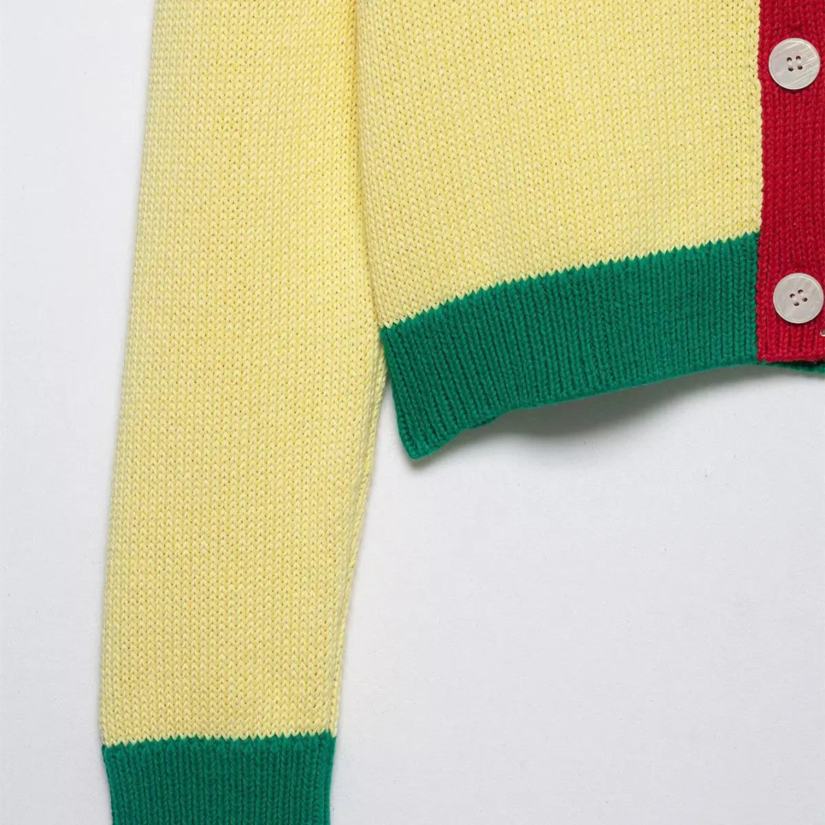 Close-up of the sleeve cuff and hem on the color-block knit cardigan, showing the green ribbed trim and white shell buttons