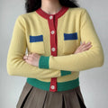 The color-block cropped knit cardigan worn by a model, showing the full silhouette, color contrast, and styling with a pleated skirt
