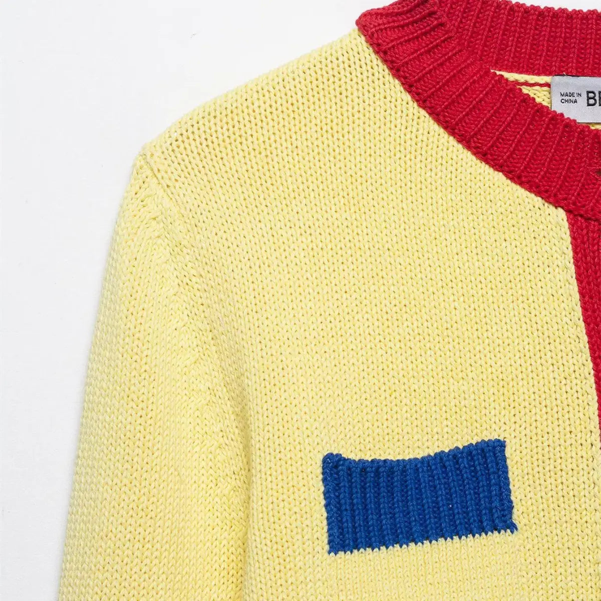 Close-up of the shoulder, neckline, and blue pocket detail on the color-block knit cardigan, showing the contrast red and blue trims