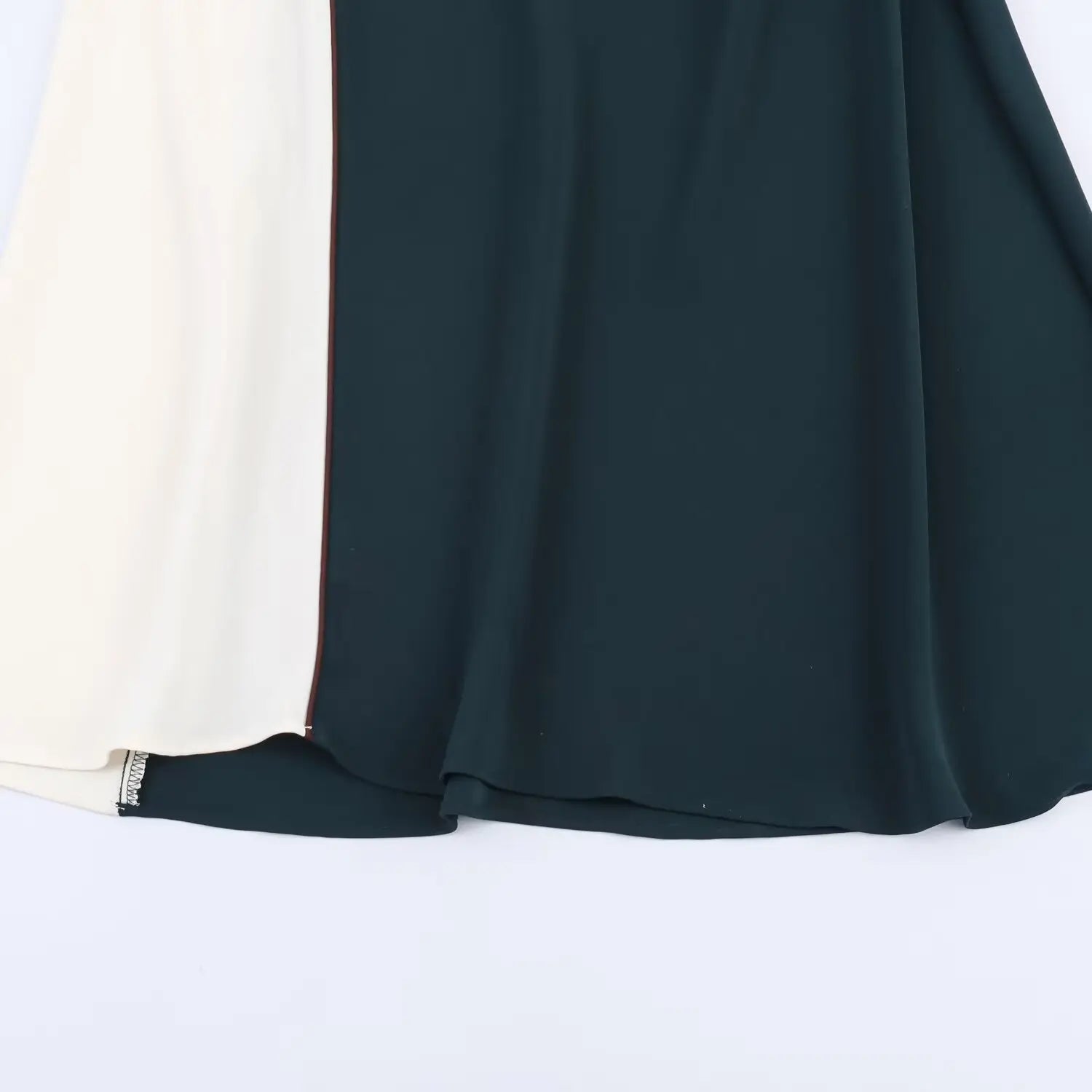 Partial shot of skirt hem, dark teal and off‑white color‑block panels, contrast piping, flowing midi hemline