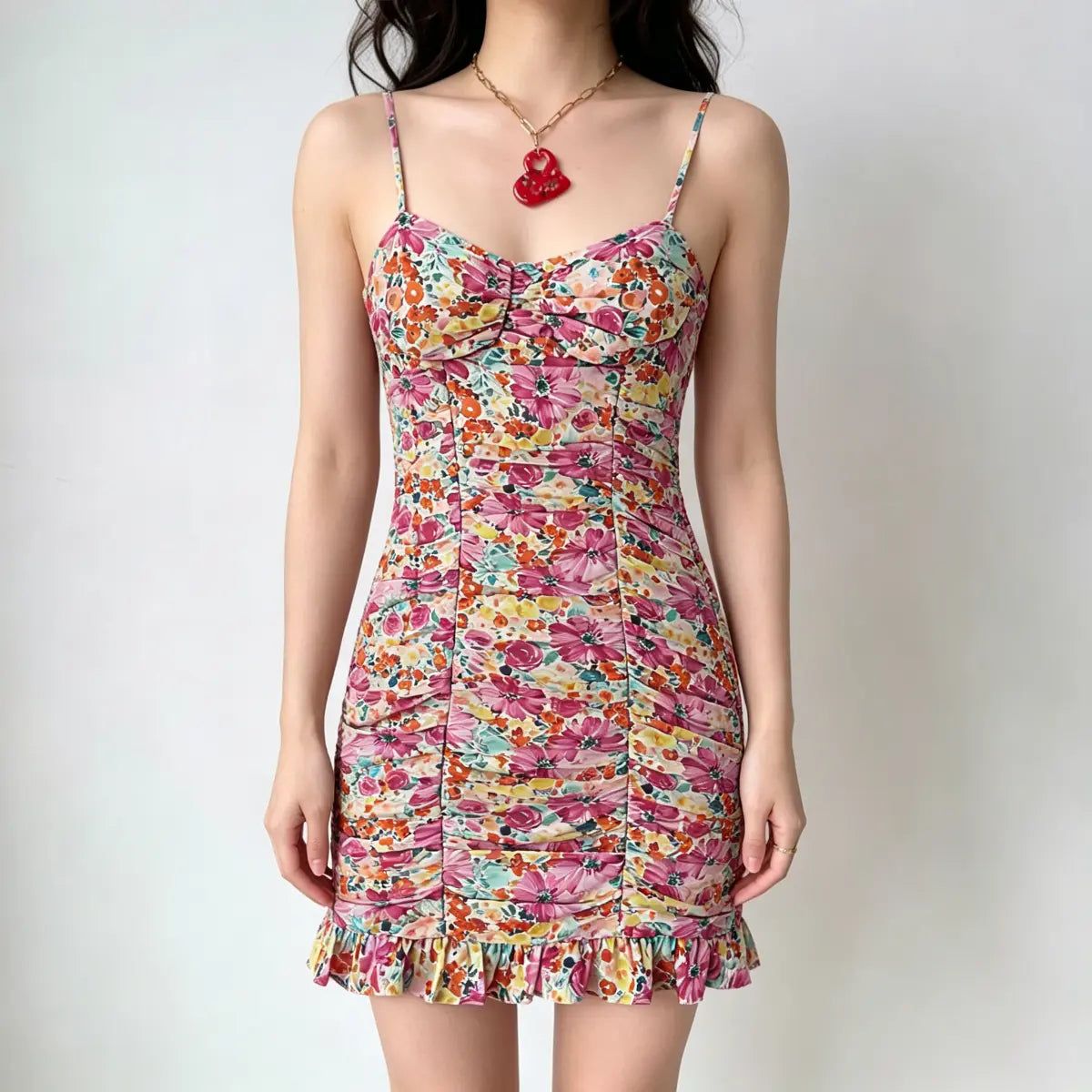Model wearing a spaghetti-strap mini dress with a vibrant watercolor floral print, ruched detailing throughout, and a ruffled hem.