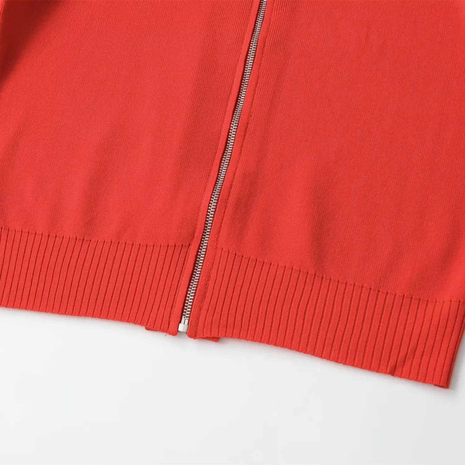 Close-up of the bottom hem, ribbed knit, and full-length zipper on the coral red top