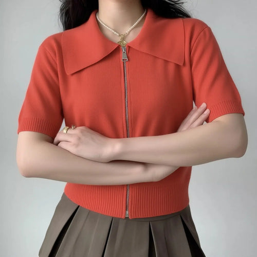 Lifestyle shot of model wearing the coral red zip-up knit top, paired with a pleated skirt, showing the cropped fit and full zipper