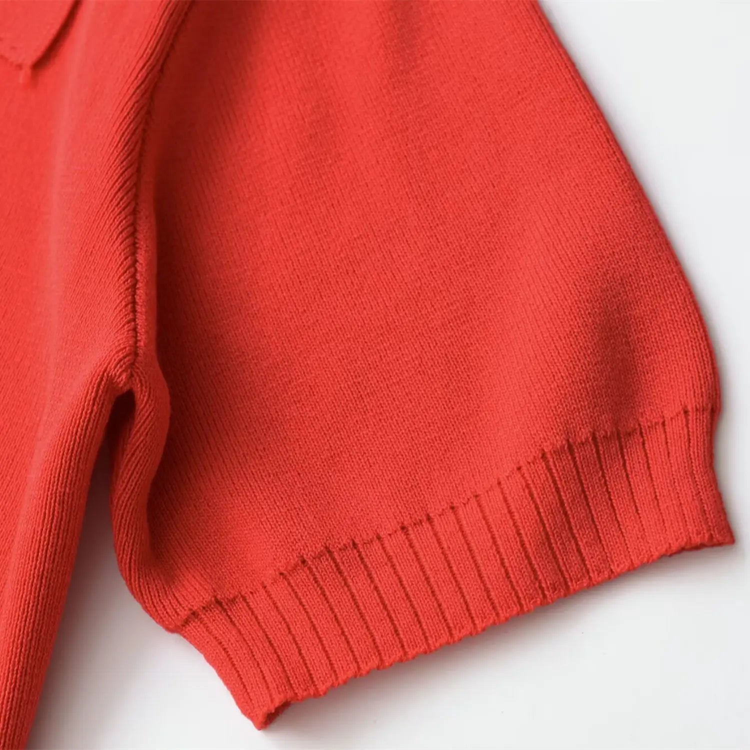 Close-up of the ribbed short sleeve cuff on the coral red zip-up knit top