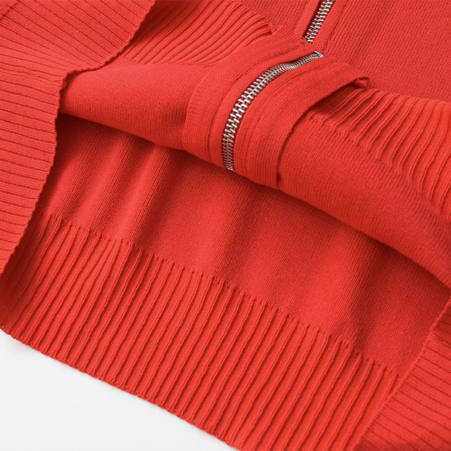 Close-up of the open zipper, showing the inner lining and ribbed hem on the coral red knit top