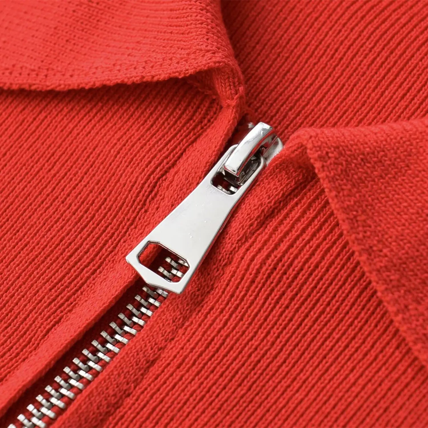 Close-up of the silver metal zipper pull and teeth on the coral red knit top