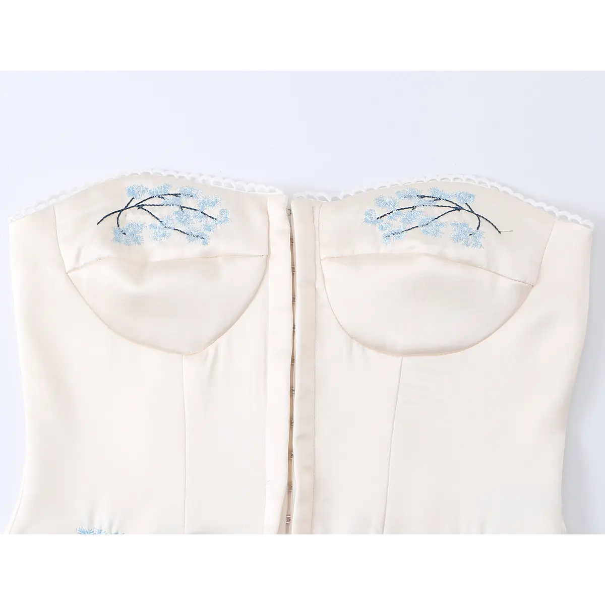 Close-up of beige corset top bust area, highlighting delicate blue floral embroidery and structured cups.