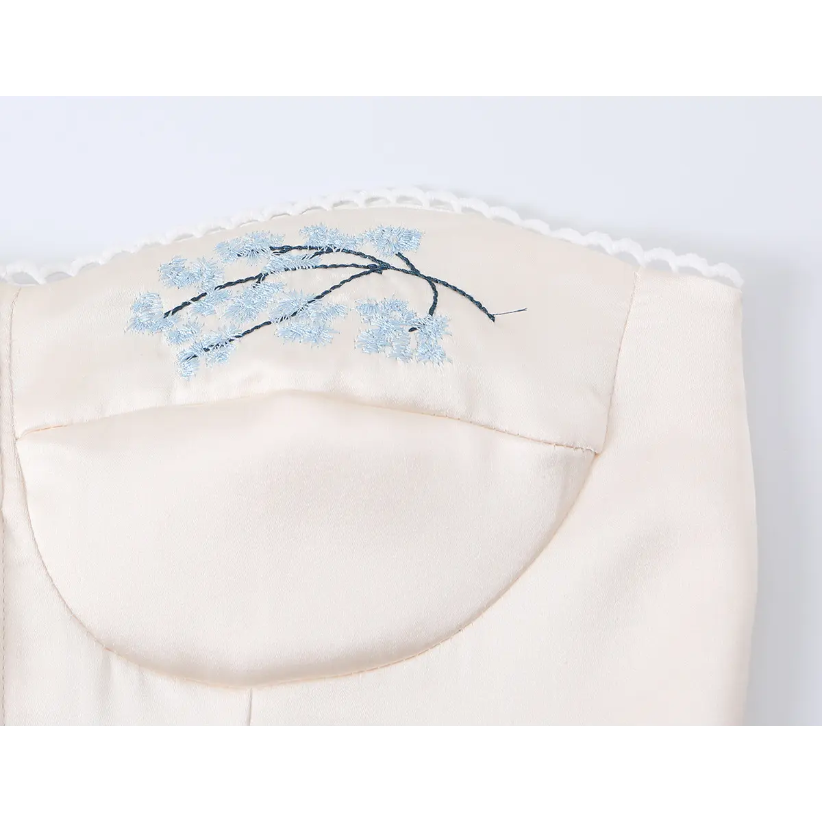 Detailed shot of blue floral embroidery on beige corset top, showing fine threadwork and lace trim.