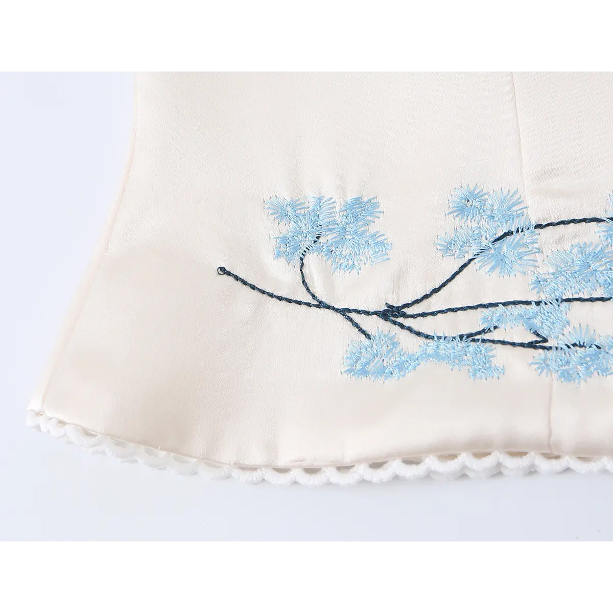 Close-up of blue floral embroidery on the bottom hem of beige corset top, highlighting intricate design details.