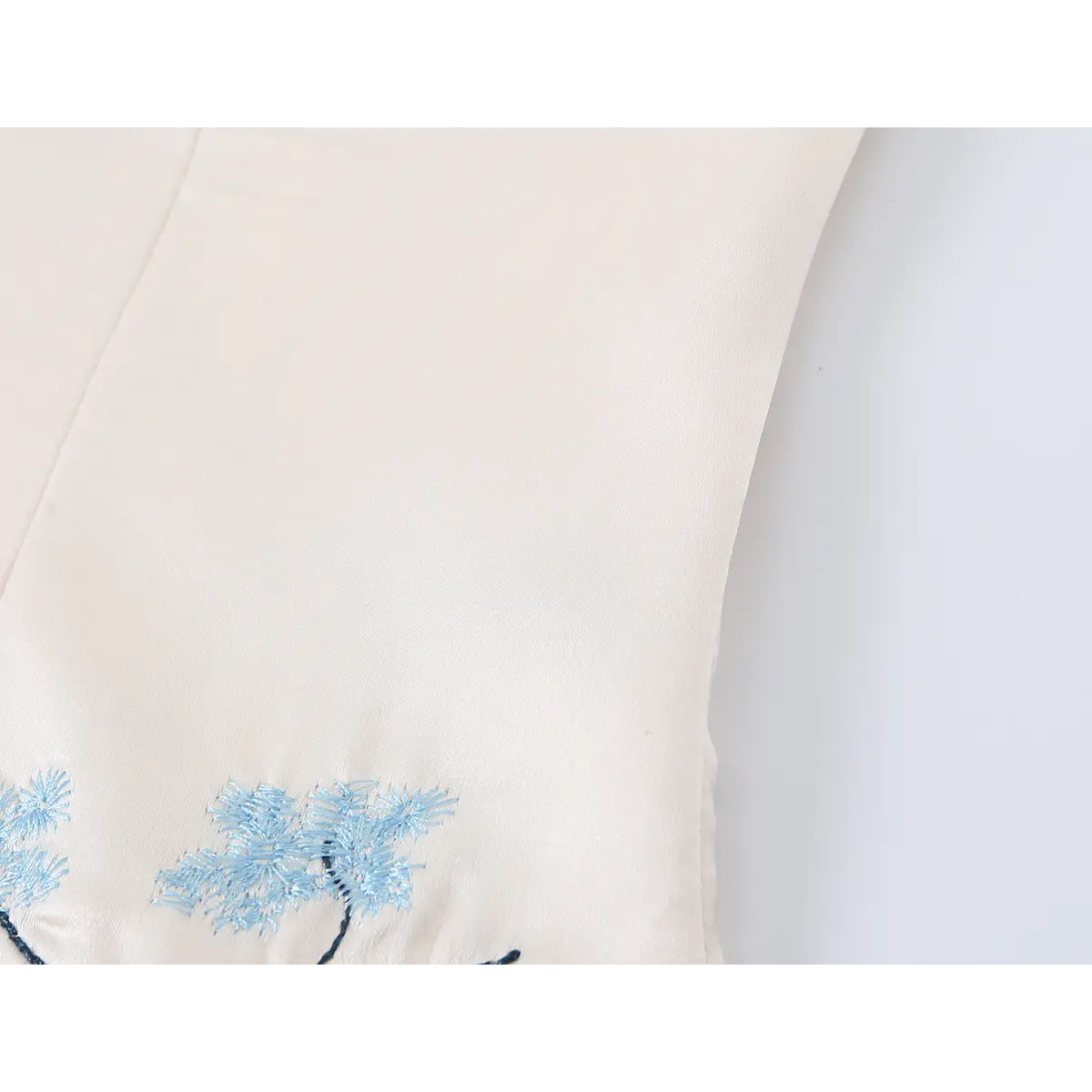 Side view detail of beige corset top, showing tailored seams and partial blue floral embroidery.
