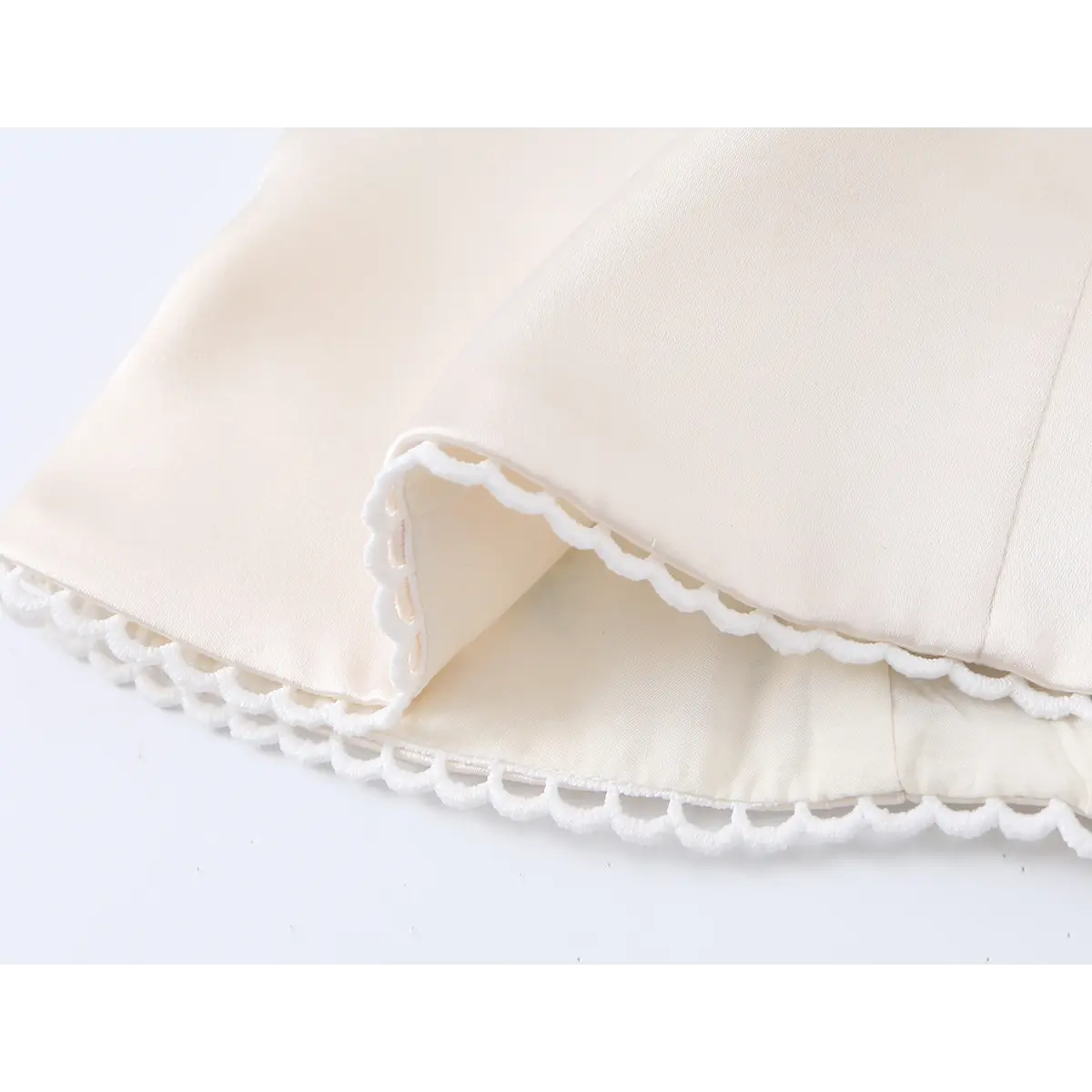 Close-up of beige corset top hem, showing scalloped lace trim and neat finished edge design.