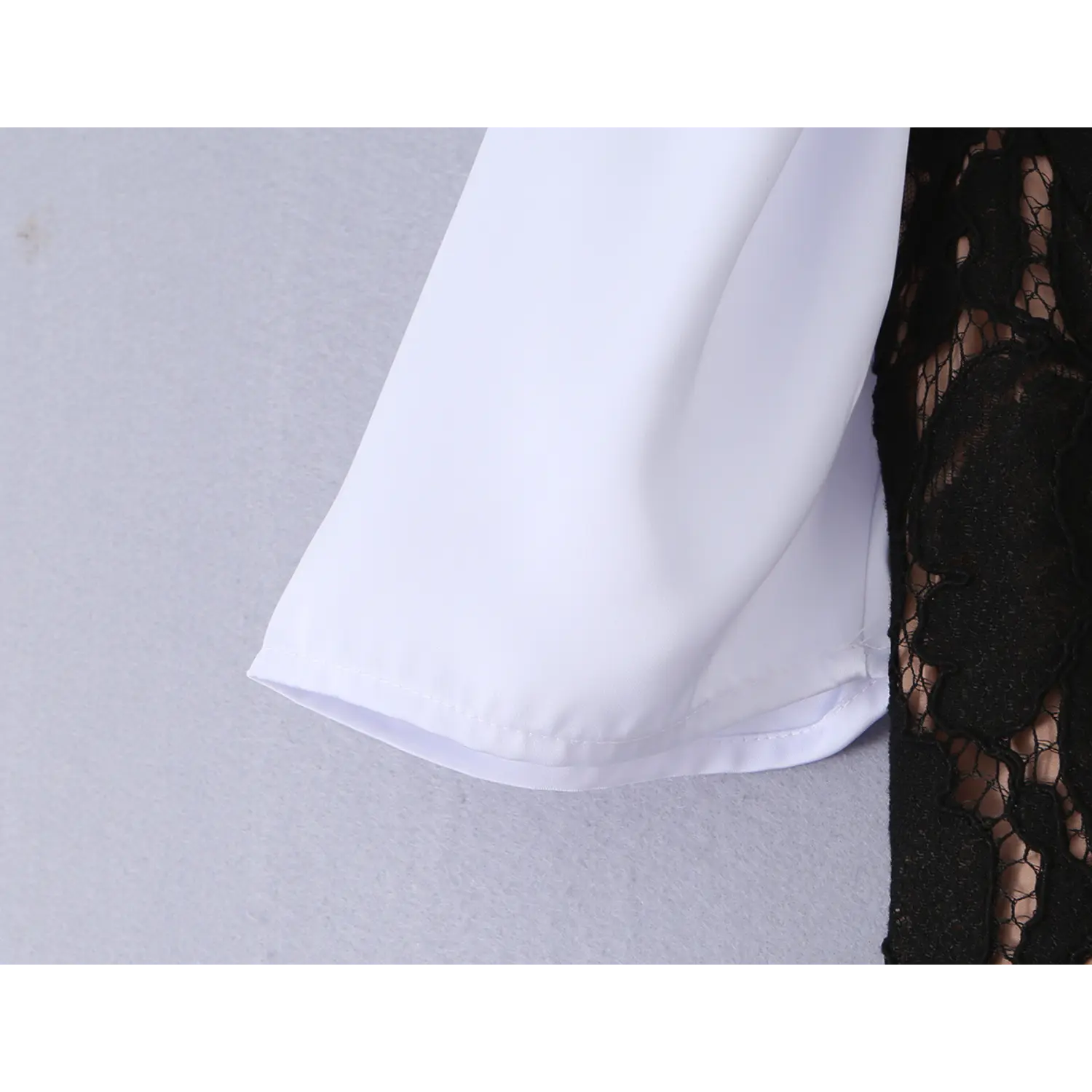 Partial close-up of smooth solid white dress sleeve hem, neat folded stitching next to black floral lace corset fabric for contrast