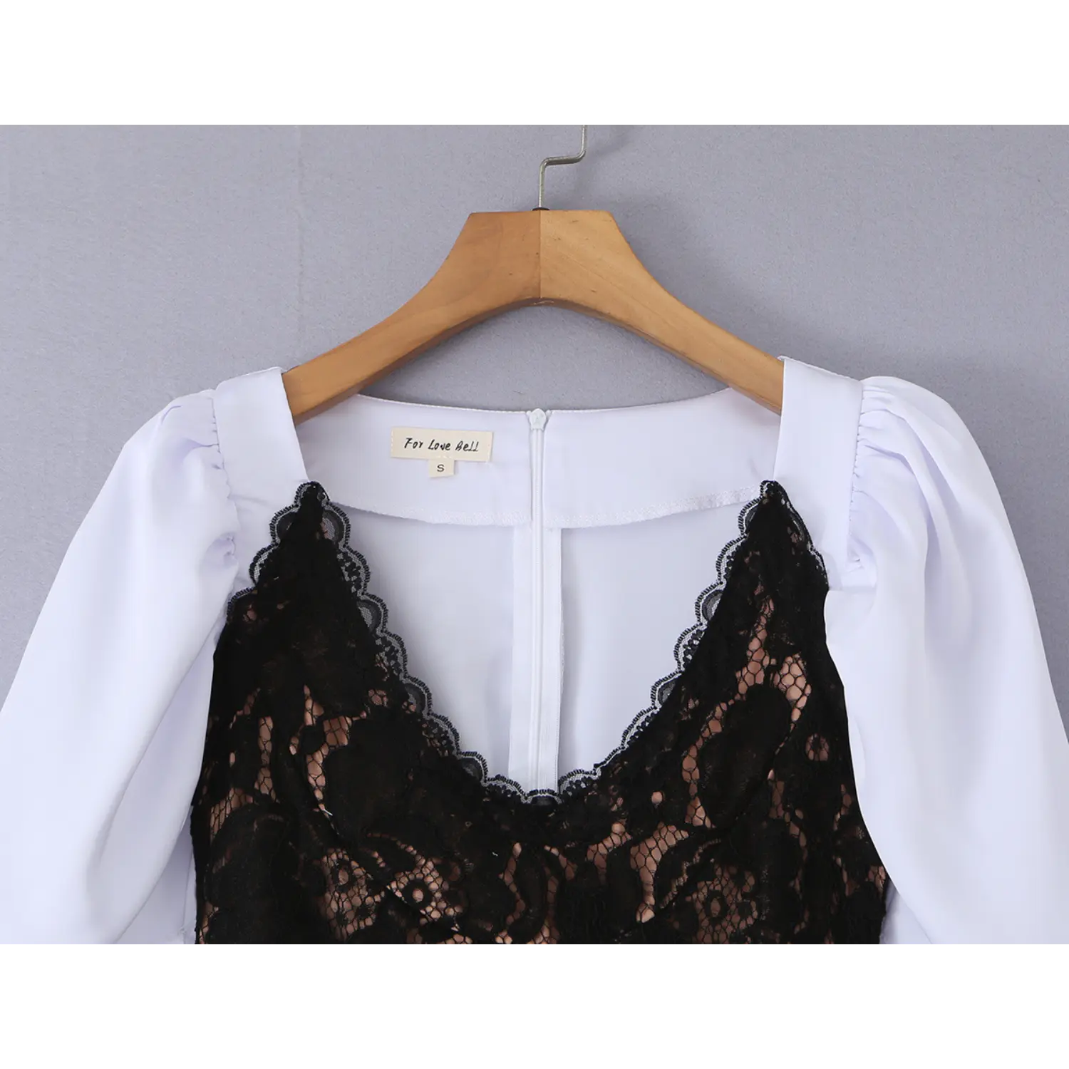 Close-up shoulder neck detail on wooden hanger, scalloped black floral lace V-neck corset overlay, inner white dress back zipper and brand size label