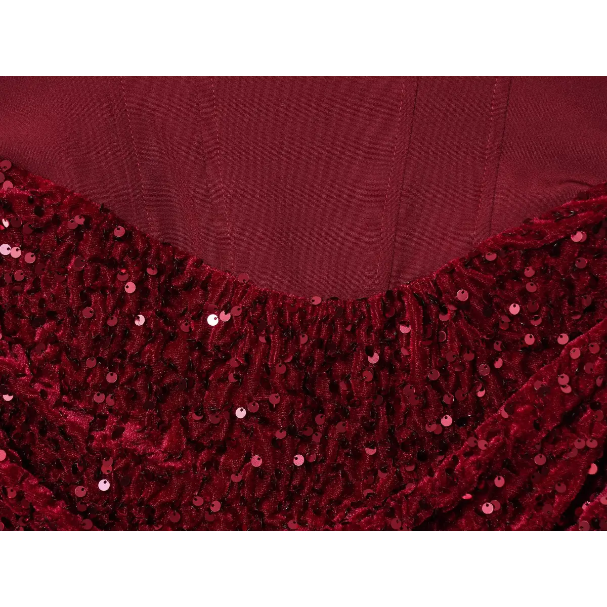 Close-up of the transition between the smooth corset bodice and the sequined velvet skirt on a wine red dress, highlighting the ruched detailing.