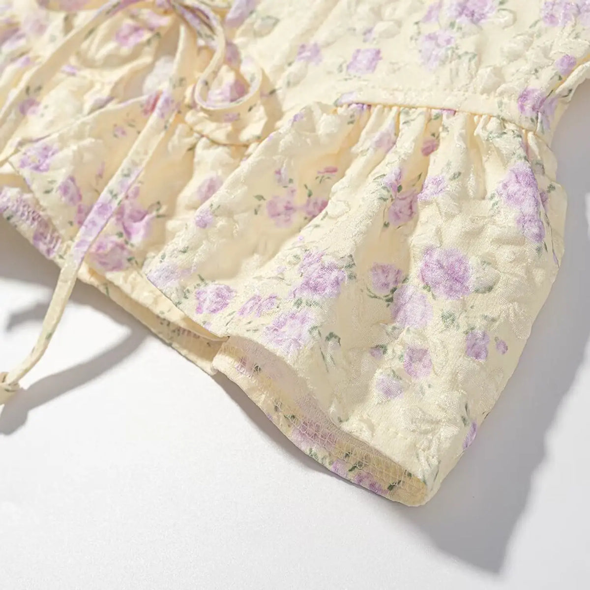 Close view of peplum hem edge, textured floral jacquard material of pale yellow purple corset cami top
