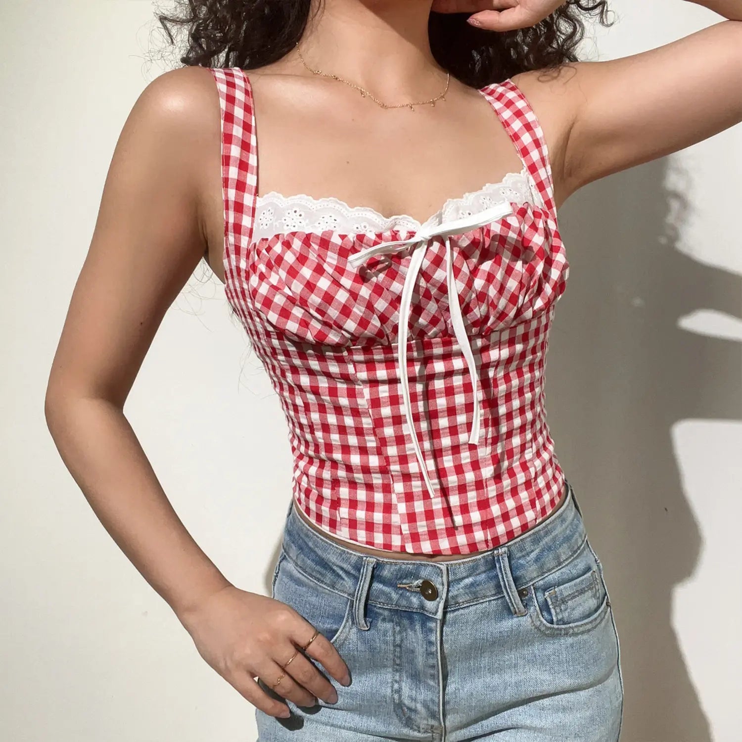 Full front lifestyle shot of model in red white checkered cropped camisole, ruched bust with white tie bow, styled with light blue casual denim jeans