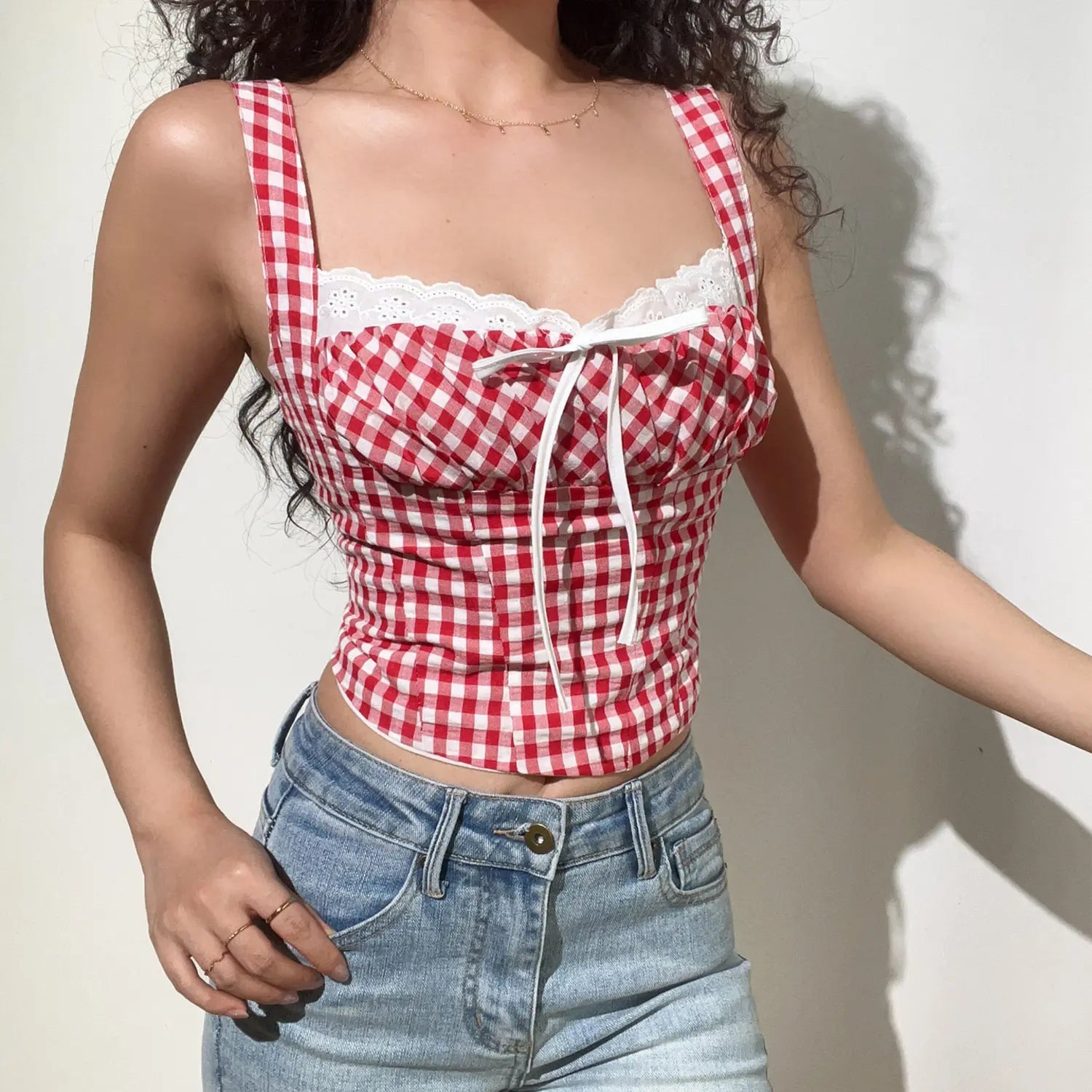 Three-quarter front lifestyle photo of gingham lace trim cami crop top, fitted corset waist, paired with classic light wash denim jeans