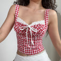 Medium close lifestyle shot of red gingham cami top with eyelet lace bust, front white ribbon tie, matching white lace hem mini skirt on model