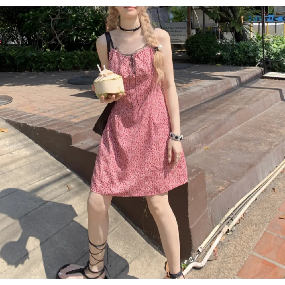 Outdoor tropical resort lifestyle shot of pink tiny floral slip mini dress, black lace trim neckline, model holding fresh coconut drink, paired with black wrap strappy sandals