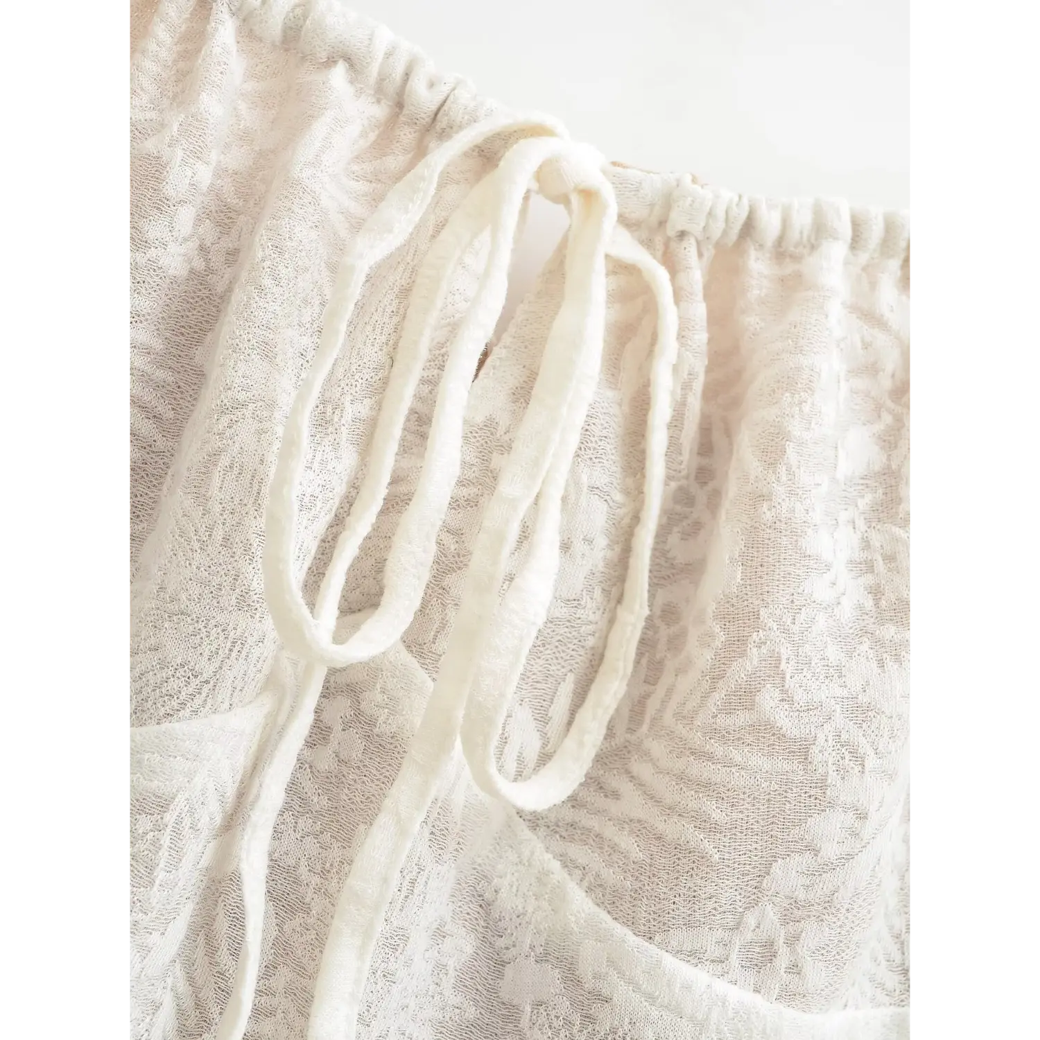 Extreme close-up of fabric drawstring tie on square neck, cream floral leaf jacquard mesh fabric with elastic ruched bust edge