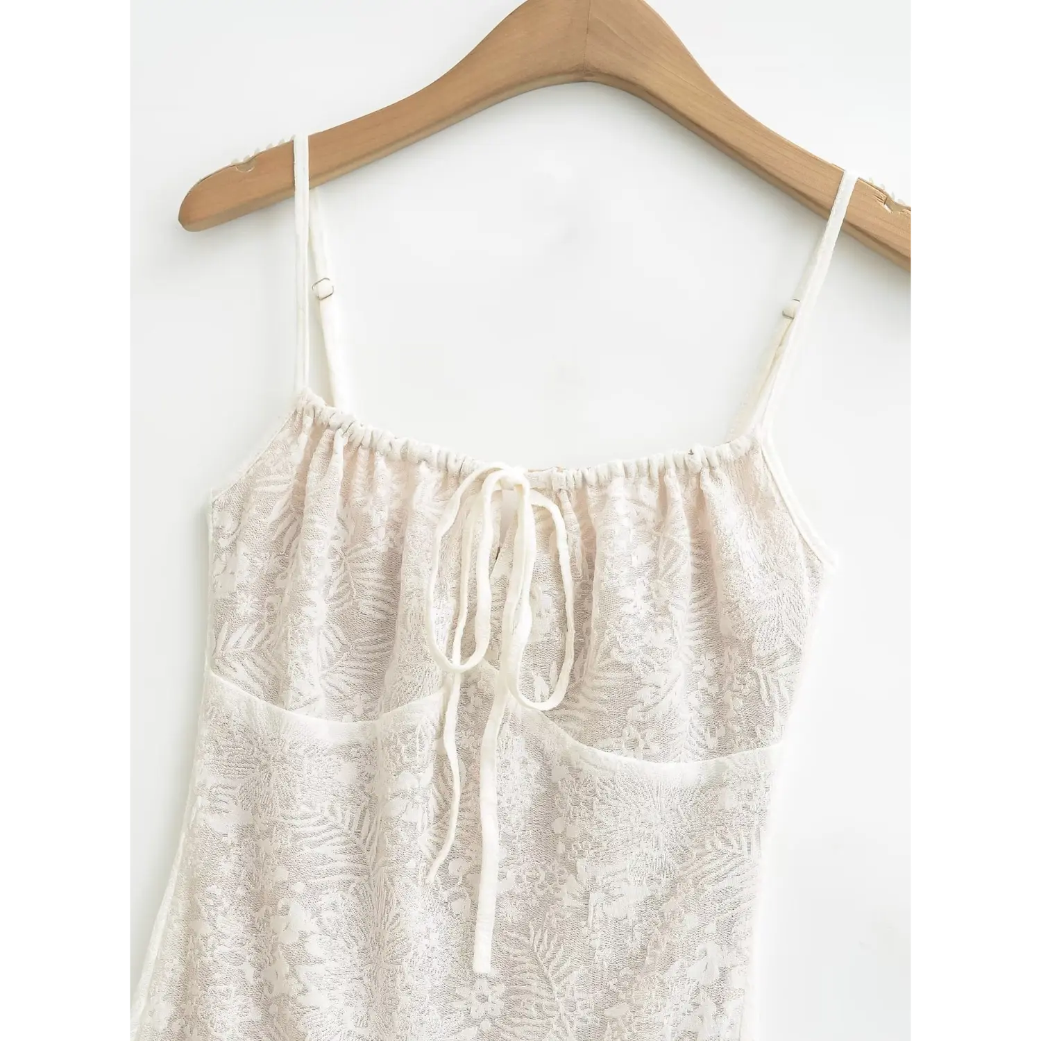 Medium close shot of square drawstring tie neck on cream jacquard slip dress, ruched bust panel and adjustable spaghetti straps on wooden hanger